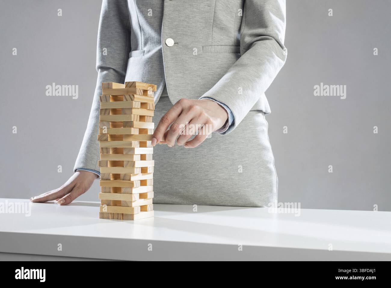 Donna d'affari che rimuove un blocco di legno dalla torre sul tavolo. Concetto di gestione dei rischi con gioco di jenga in legno. Sviluppo aziendale e assistenza. Nuovo Foto Stock