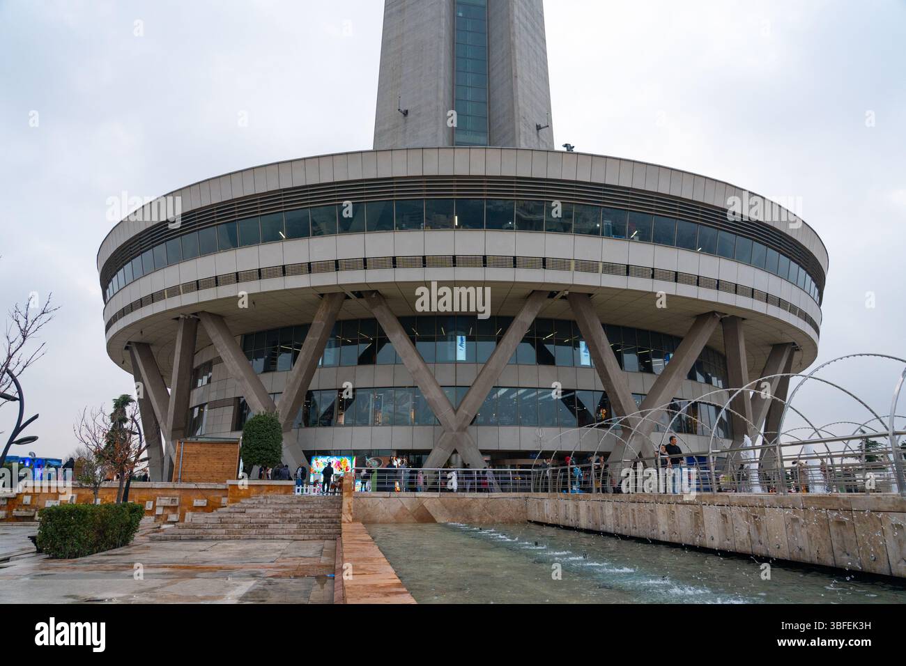 Teheran, Iran - 12 novembre 2023: La base della Milad Tower con visitatori e fontana nella piazza pubblica Foto Stock