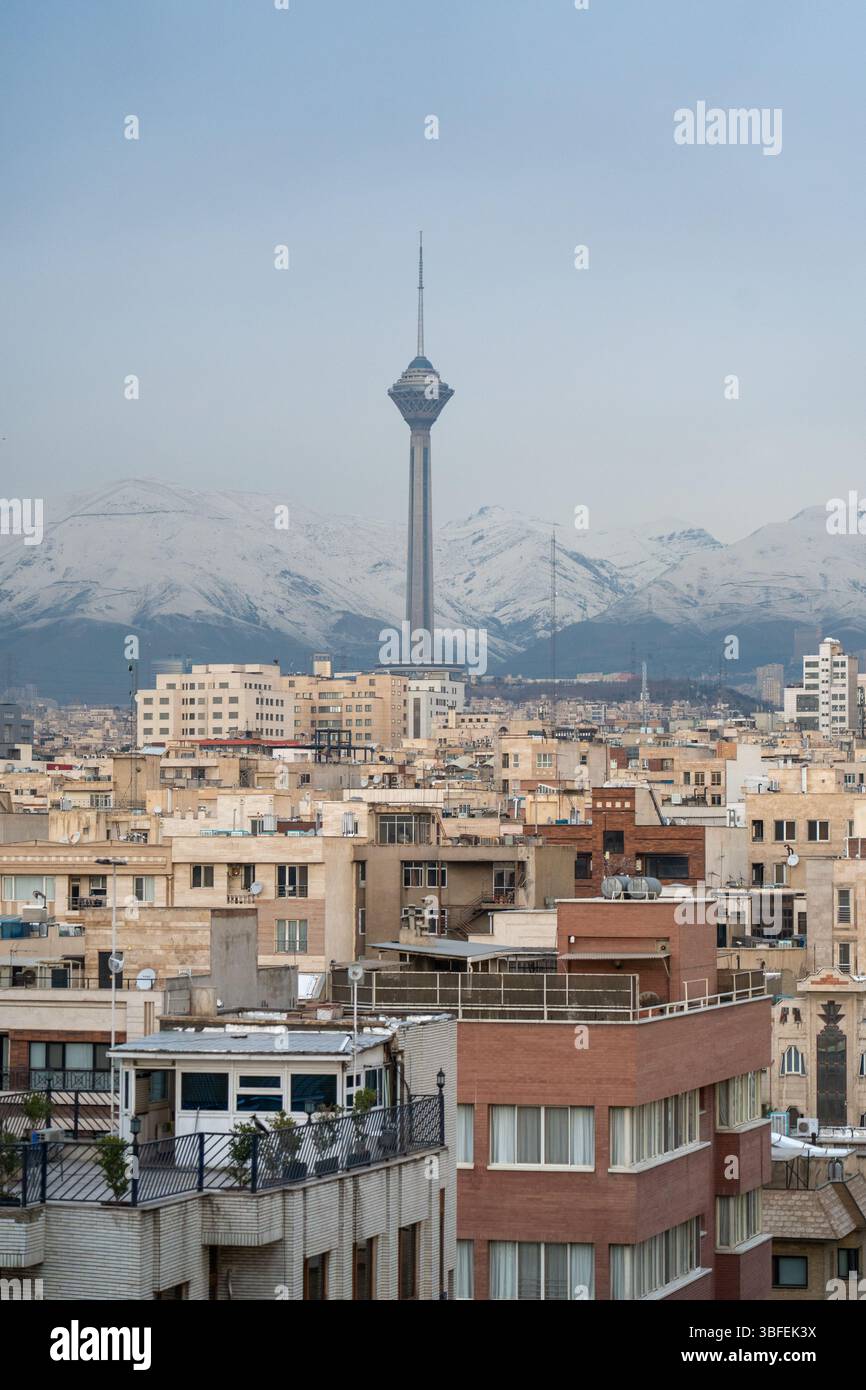 Teheran, Iran - 12 novembre 2023: Vista ravvicinata della Milad Tower sopra i tetti con montagne sullo sfondo Foto Stock