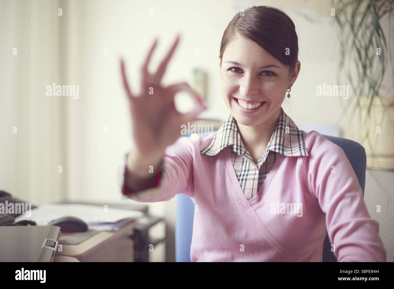 Ritratto di giovane donna d'affari caucasica in gilet rosa nel suo ufficio che mostra il segno ok Foto Stock