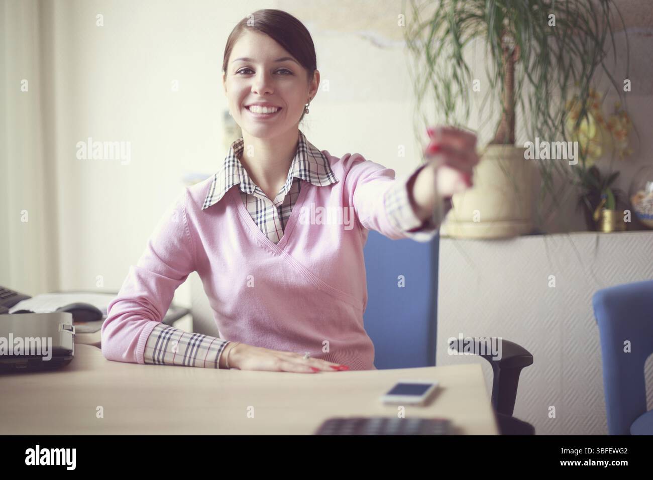 Ritratto della giovane donna d'affari caucasica in gilet rosa nel suo ufficio che dà le chiavi Foto Stock