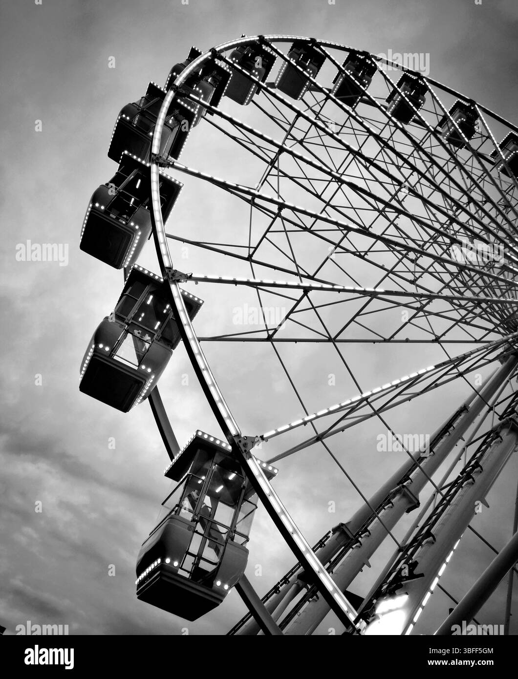 Una grande ruota panoramica si erge in modo prominente su uno sfondo di nuvole e le sue cabine illuminate mostrano un'atmosfera divertente in un parco divertimenti. Foto Stock