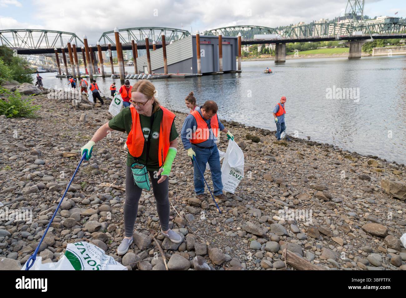 Portland, Oregon - 17 agosto 2017: Volontari che ripuliscono la spazzatura lungo la riva del fiume, indossando giubbotti arancioni e usando le pinze per raccogliere i rifiuti. Foto Stock