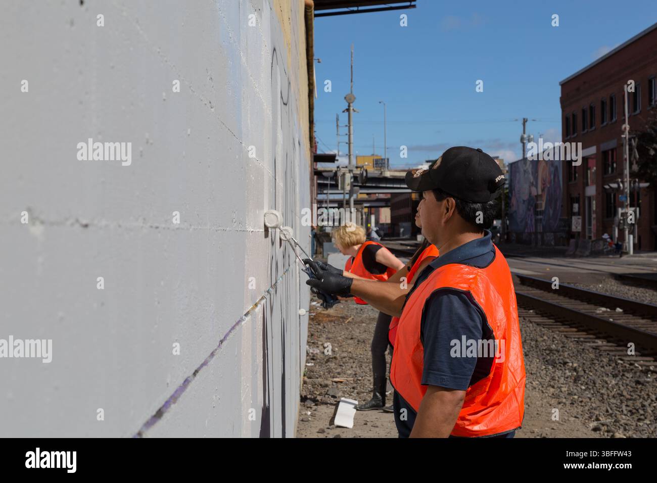 Portland, Oregon - 17 agosto 2017: I volontari dipingono graffiti su un muro vicino ai binari del treno, migliorando l'aspetto della comunità. Foto Stock