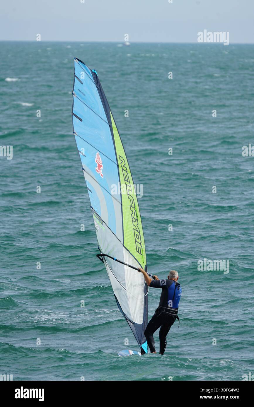 Windsurfer professionista che naviga attraverso le acque turchesi dell'oceano in un giorno di sole. Hayling Island, Regno Unito Foto Stock