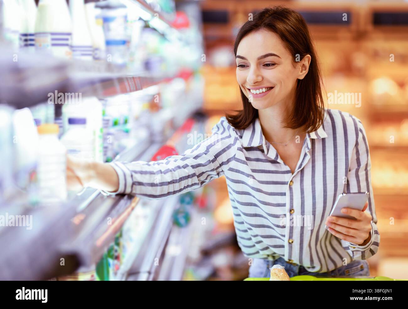 Donna che tiene lo smartphone in piedi in negozio prendendo il latte Foto Stock