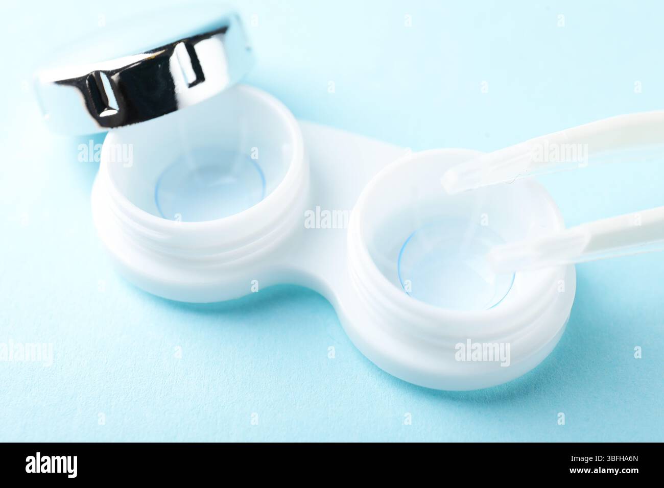 Lenti a contatto nella custodia e pinzette su sfondo azzurro, primo piano Foto Stock