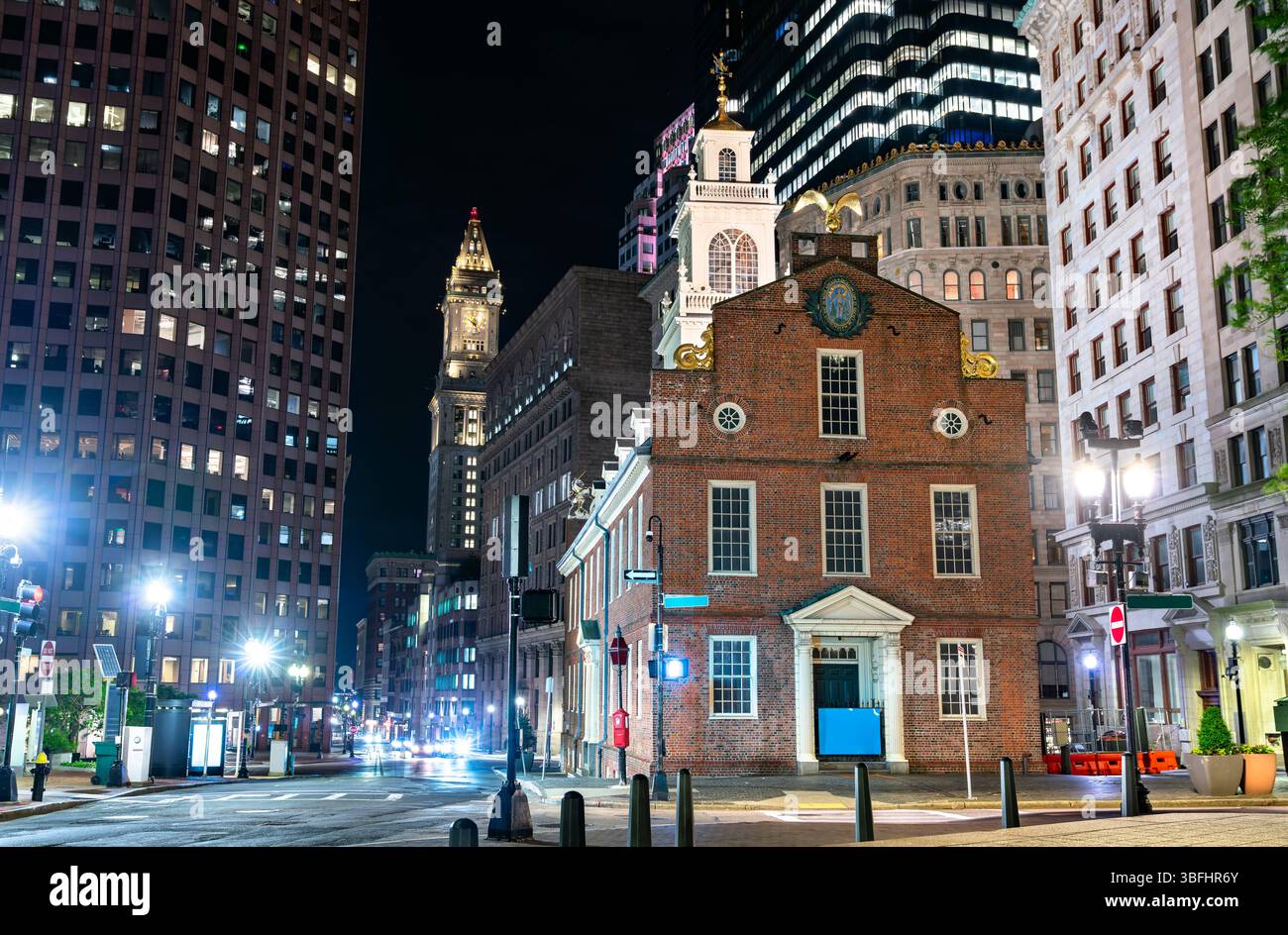 Vista notturna della storica Old State House di Boston, Massachusetts, circondata da grattacieli moderni e da lampioni delicatamente illuminati. L'edificio di epoca coloniale si distingue per la sua facciata in mattoni rossi e l'iconico balcone, che segna un sito significativo nella storia americana Foto Stock