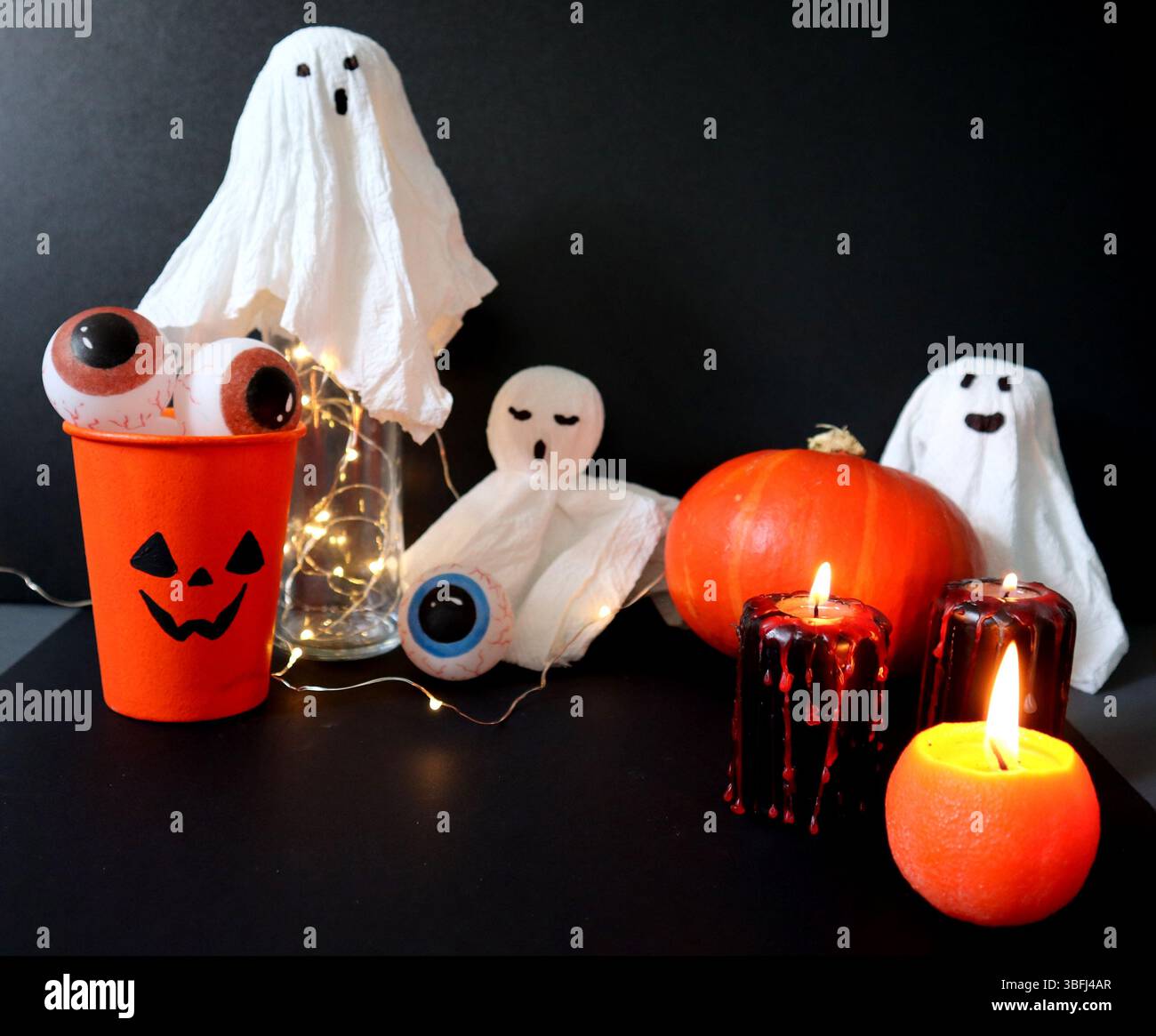 Set di vari elementi per Halloween. Il vetro Jack o lanterna è pieno di occhi. Candele arancioni e nere con gocce rosse. Zucca. Giocattoli piccoli fantasmi W Foto Stock