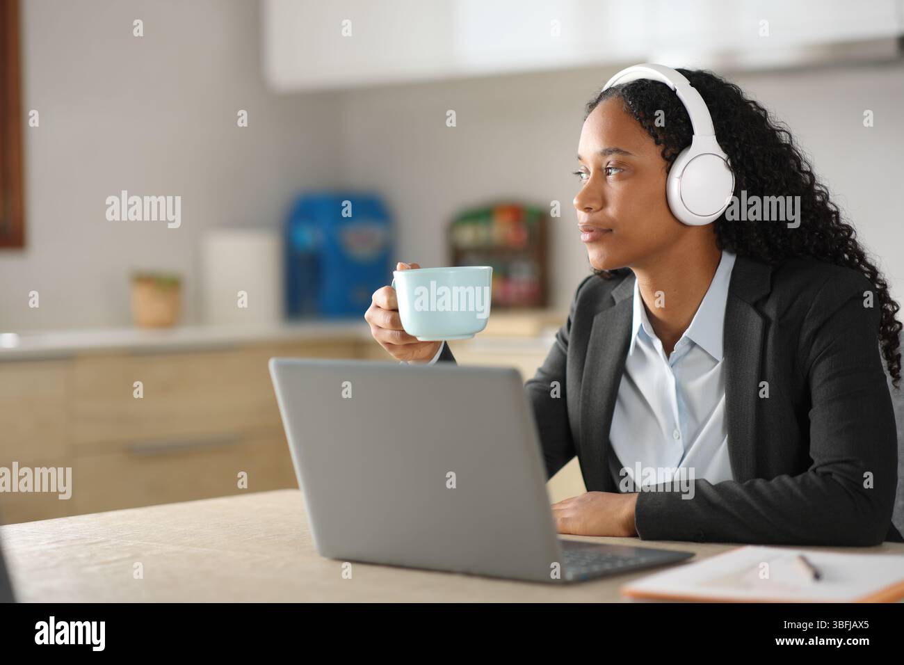 Un dirigente nero ascolta l'audio online bevendo in cucina a casa Foto Stock