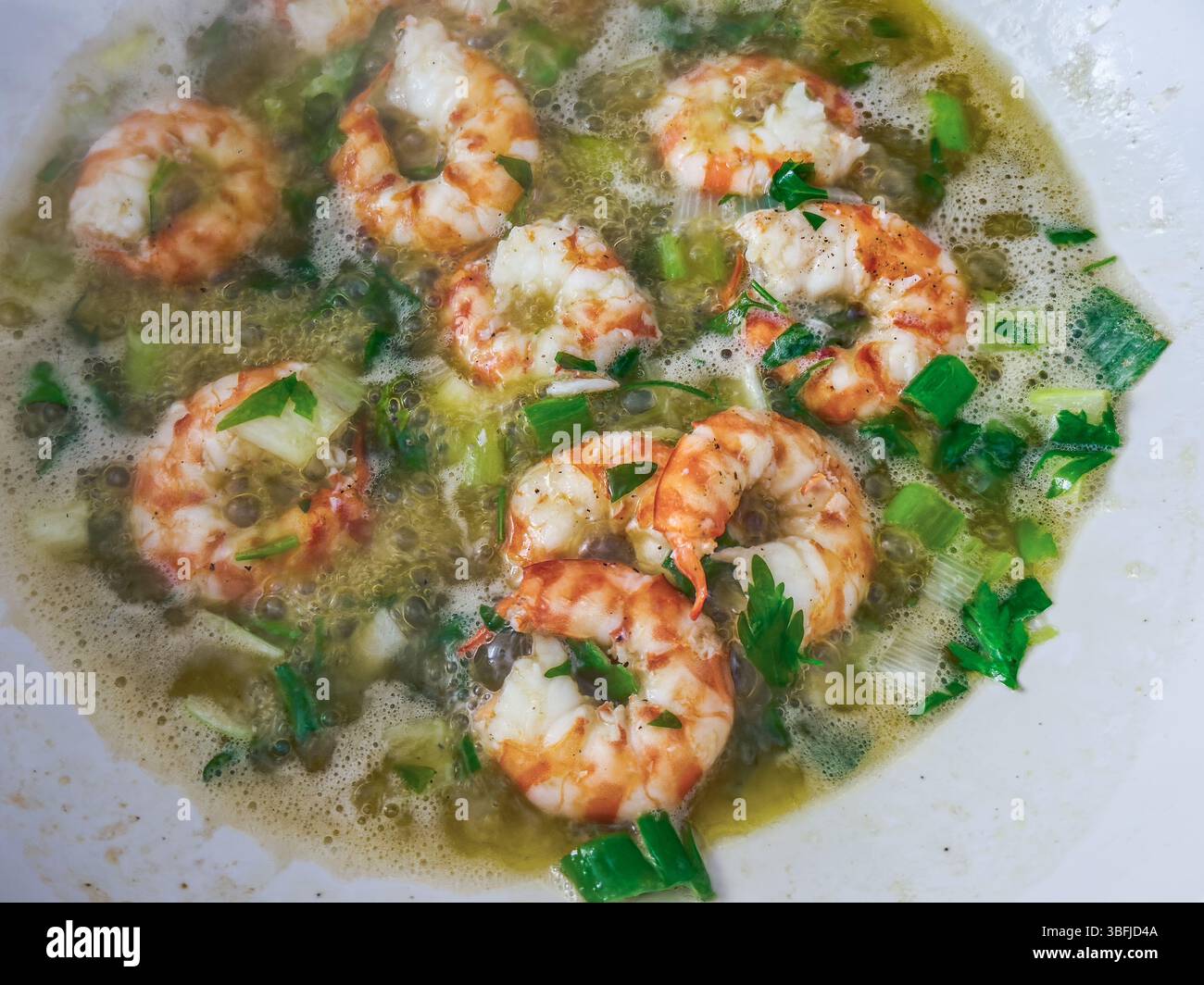 I succosi gamberi sospesi in un brodo gorgogliante accanto a verdure verdi ed erbe aromatiche, creando una deliziosa esperienza culinaria in una cucina allegra. Foto Stock