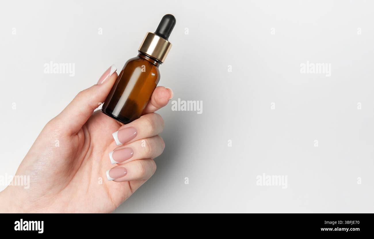 L'estetista tiene in mano il flacone contagocce in vetro ambrato con elementi dorati su sfondo bianco e spazio di copia Foto Stock
