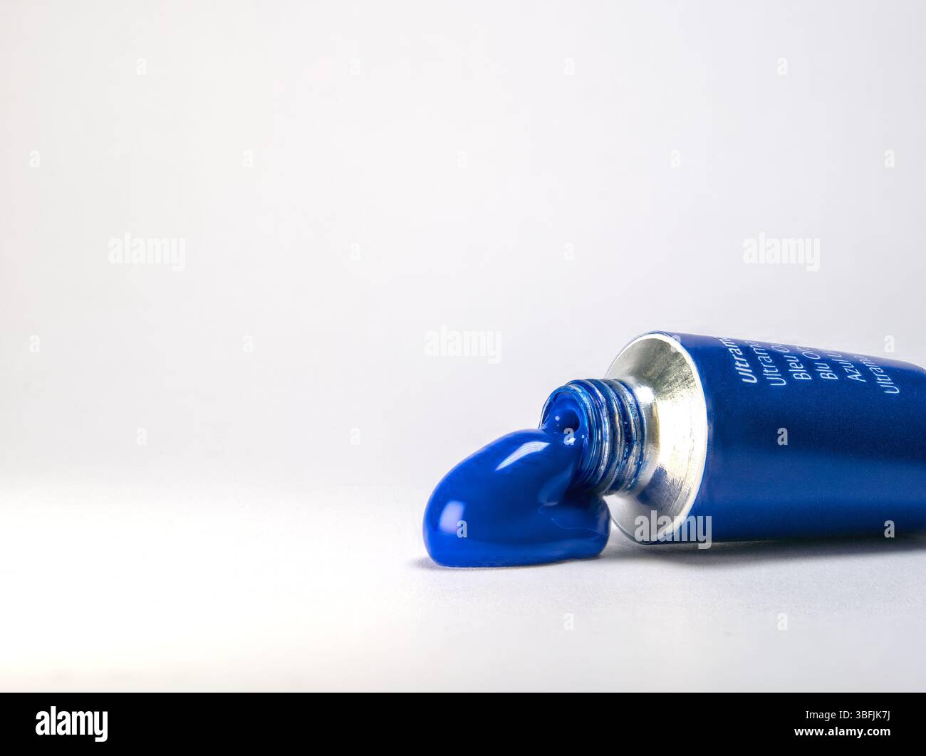 Un primo piano di un tubo di vernice blu ultramarina con una piccola quantità di vernice blu brillante strizzata su una superficie bianca pulita Foto Stock