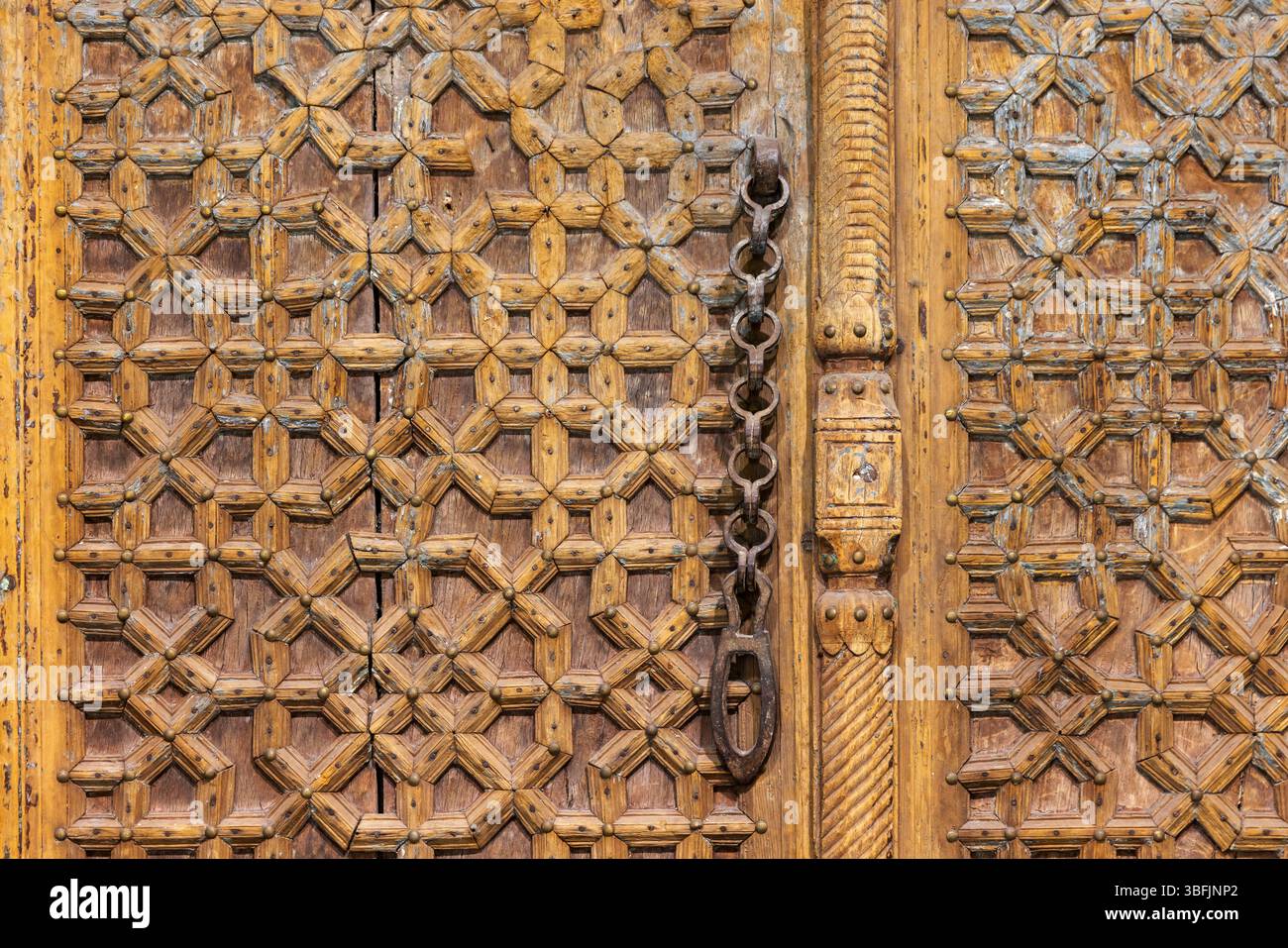 Vista dettagliata di una porta in legno caratterizzata da intricate incisioni geometriche e una catena metallica. Mette in risalto l'artigianato tradizionale e il design culturale Foto Stock