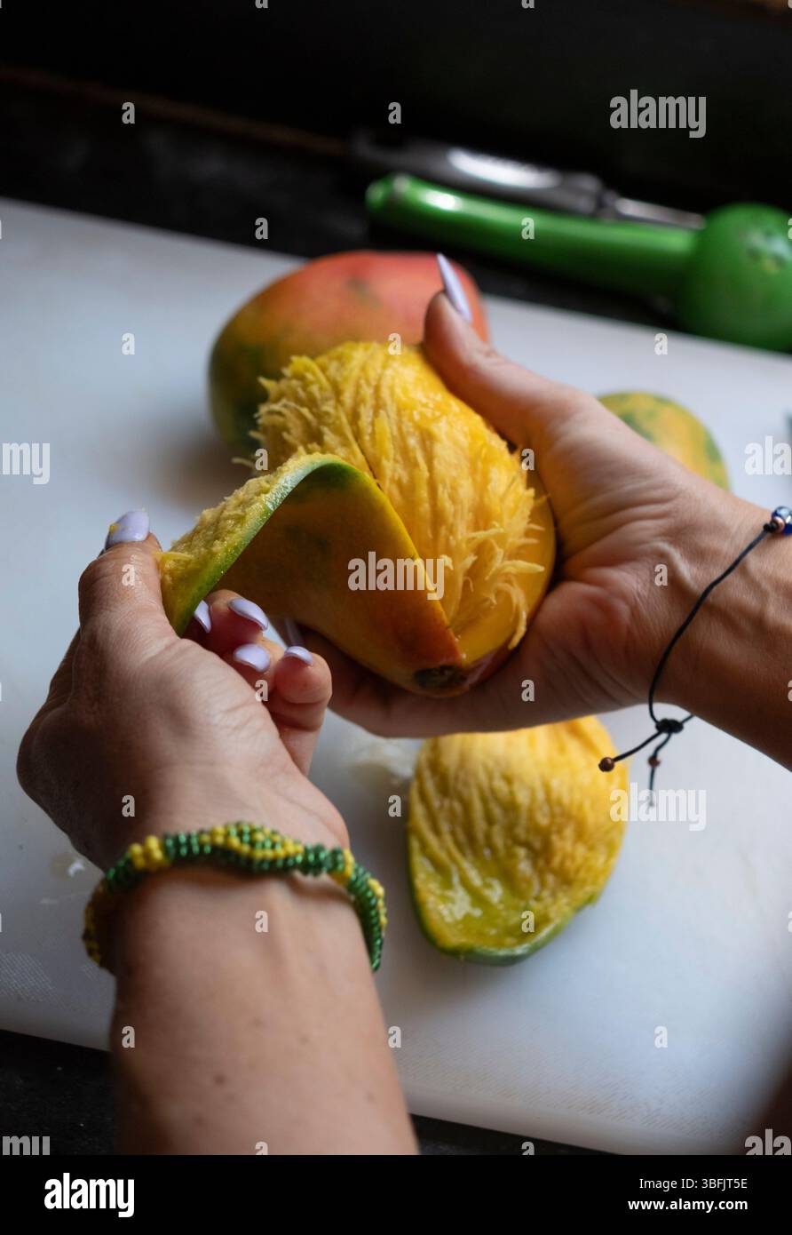 Donna che sbuccia il mango fresco sul tagliere Foto Stock