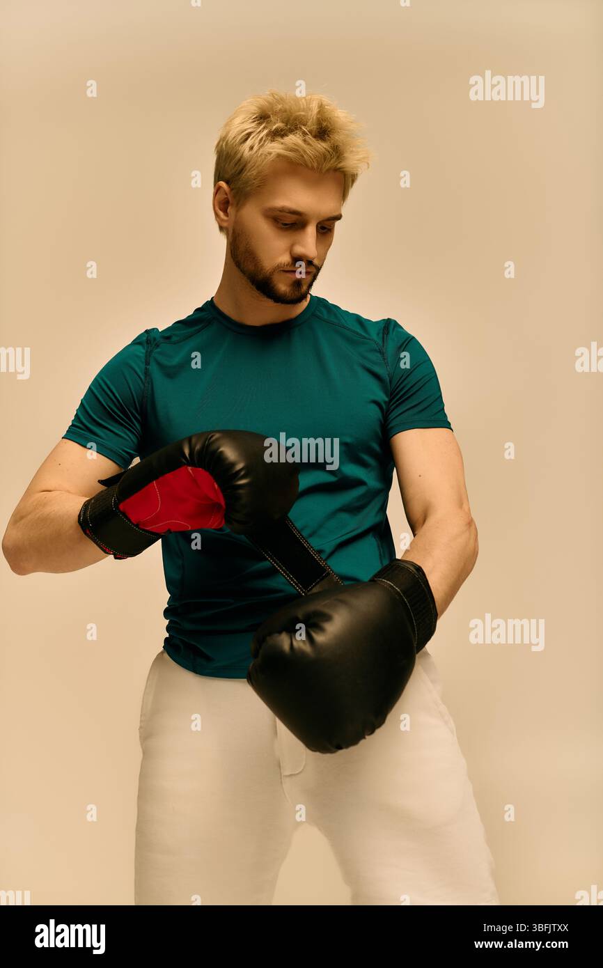 Il giovane con una camicia color verde acqua si concentra sui guanti da boxe mentre si prepara per la sua sessione di allenamento. Foto Stock