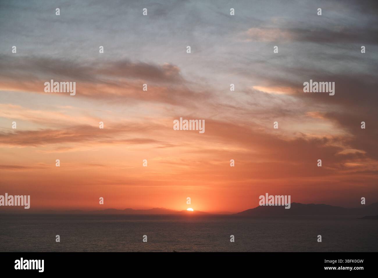 Una serena vista del tramonto sull'oceano con cieli nebbiosi e morbide nuvole che creano un'atmosfera da sogno. Foto Stock