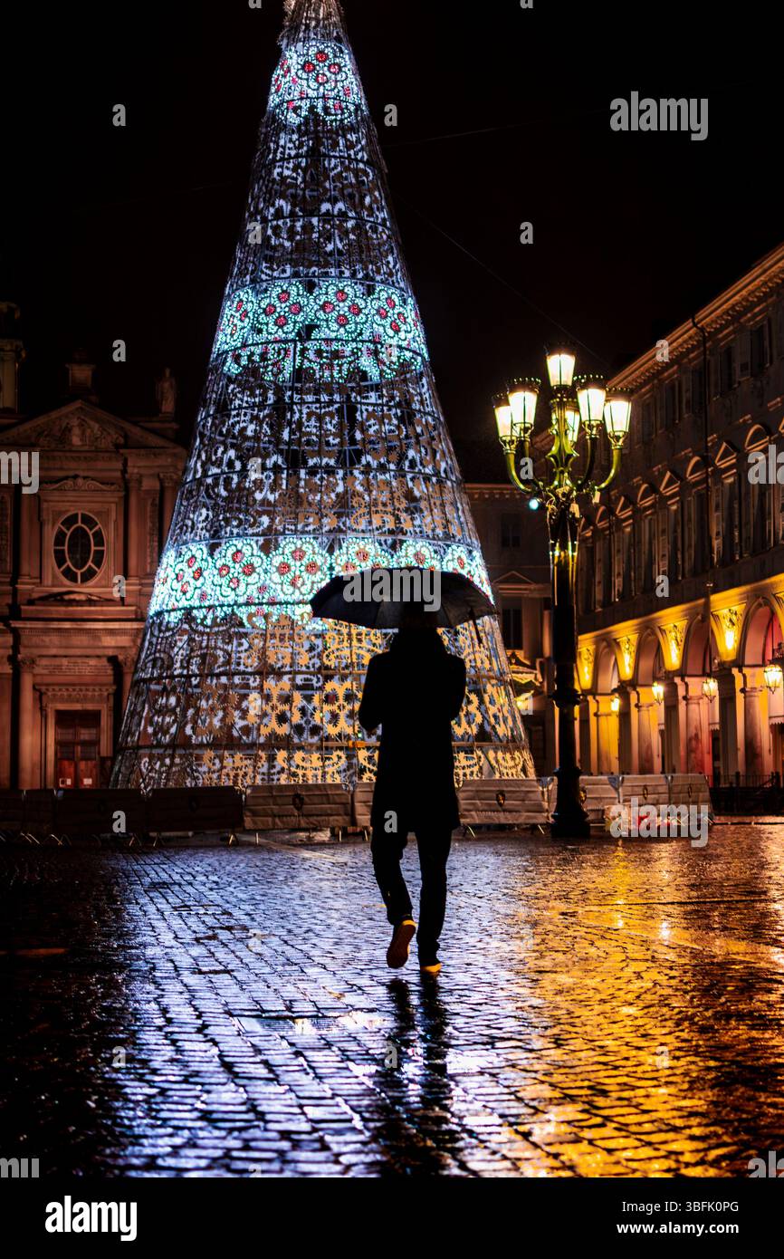 Silhouette di un uomo con l'ombrello che guarda l'albero di Natale in Piazza San Carlo, nel cuore di Torino. Foto Stock