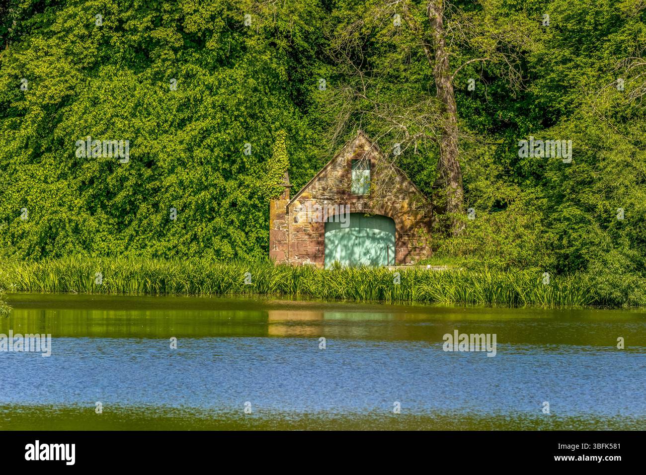 Vecchia casetta sul bordo del Fyvie loch circondata da alberi Foto Stock
