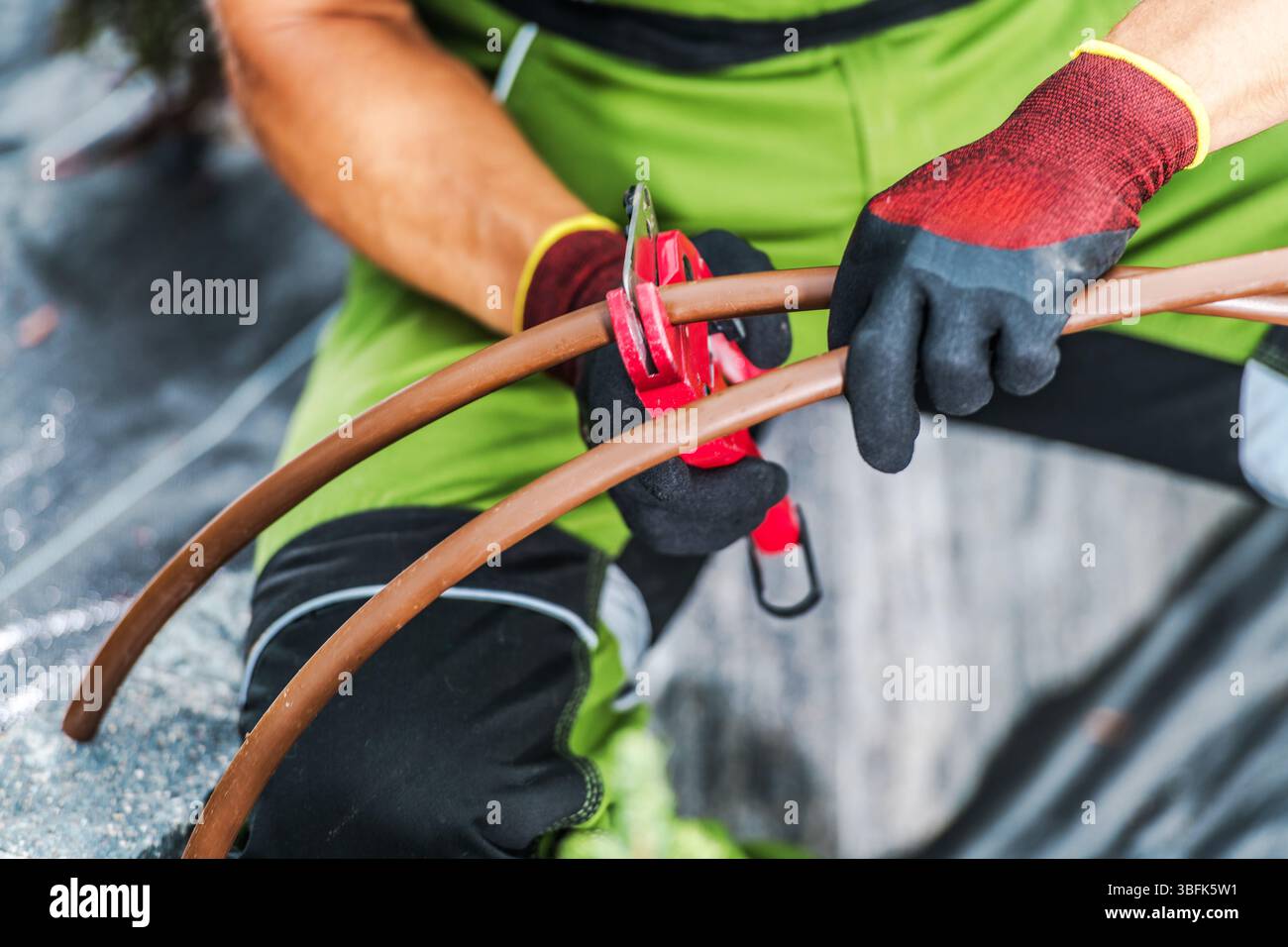 Un lavoratore dedicato si concentra sul taglio delle tubazioni utilizzando gli strumenti appropriati in un cantiere edile all'aperto durante le ore diurne. Foto Stock