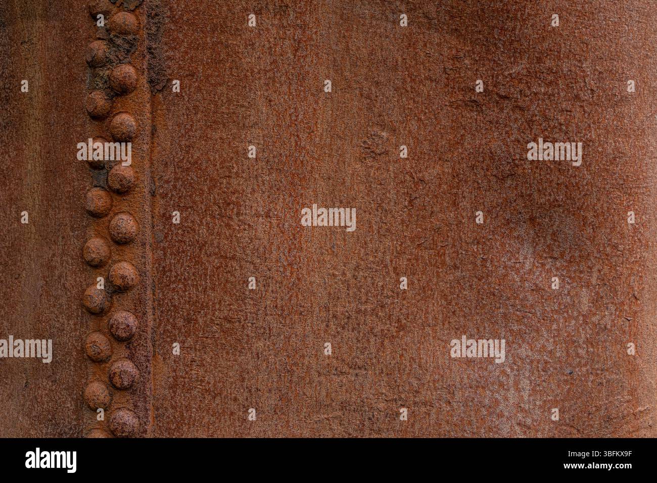 Primo piano di una superficie in acciaio arrugginito con file verticali di rivetti e consistenza di forte corrosione Foto Stock