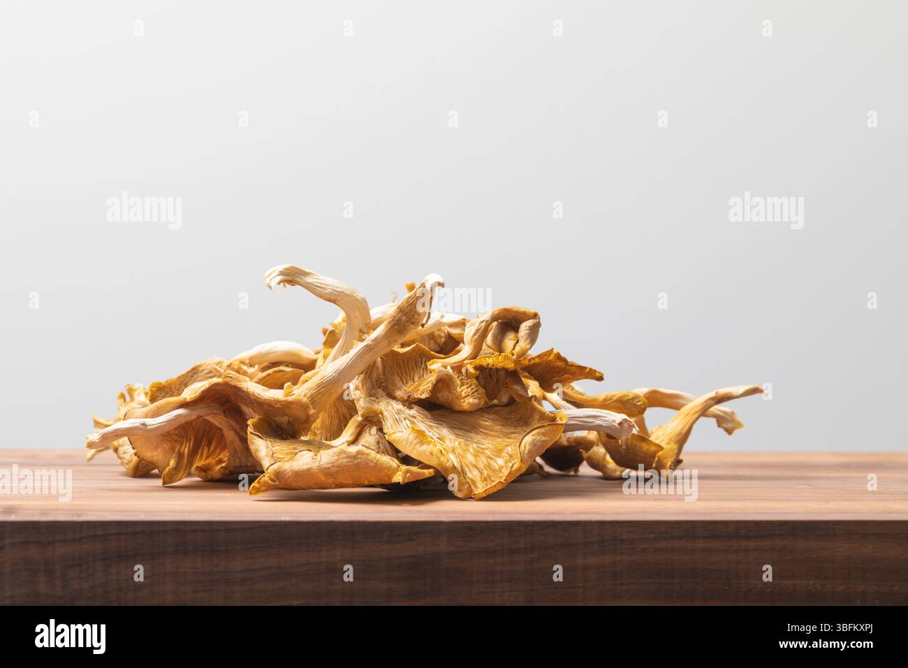Mucchio di funghi ostrici essiccati su tagliere in legno con luce da studio luminosa, che mostra una consistenza naturale e un ingrediente culinario biologico Foto Stock