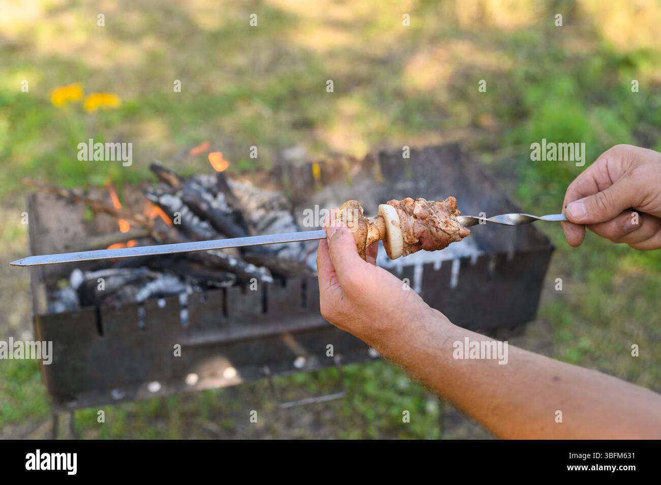 Mani che assemblano shish kebab con cura, alternando carne e verdure. fase di preparazione di un delizioso shashlik. mans mani afferrano spiedino, caricandolo Foto Stock