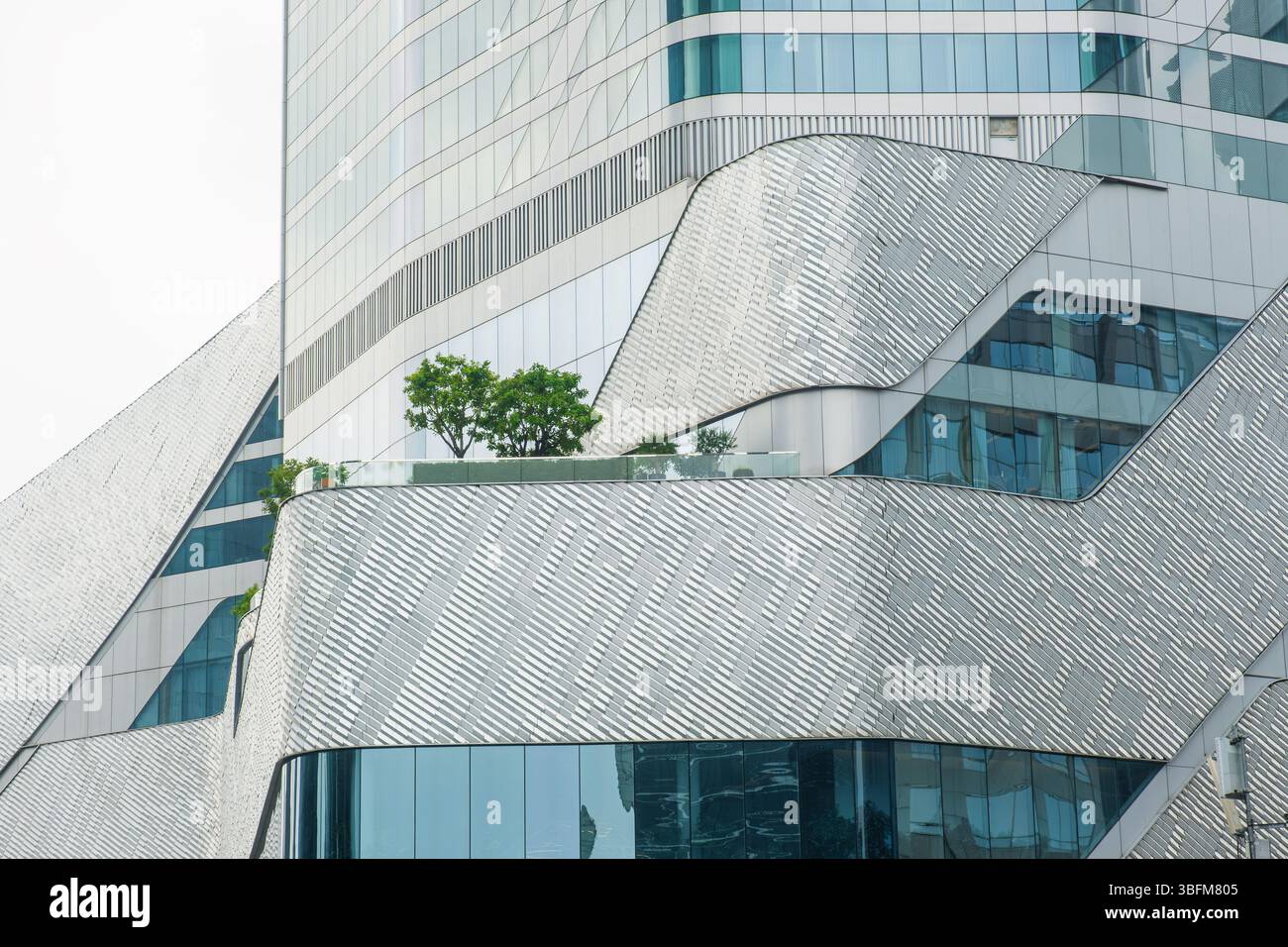 Dettagli di architettura moderna con elegante facciata curva in vetro e metallo, motivi argentati testurizzati, piante verdi da giardino, design futuristico contemporaneo Foto Stock