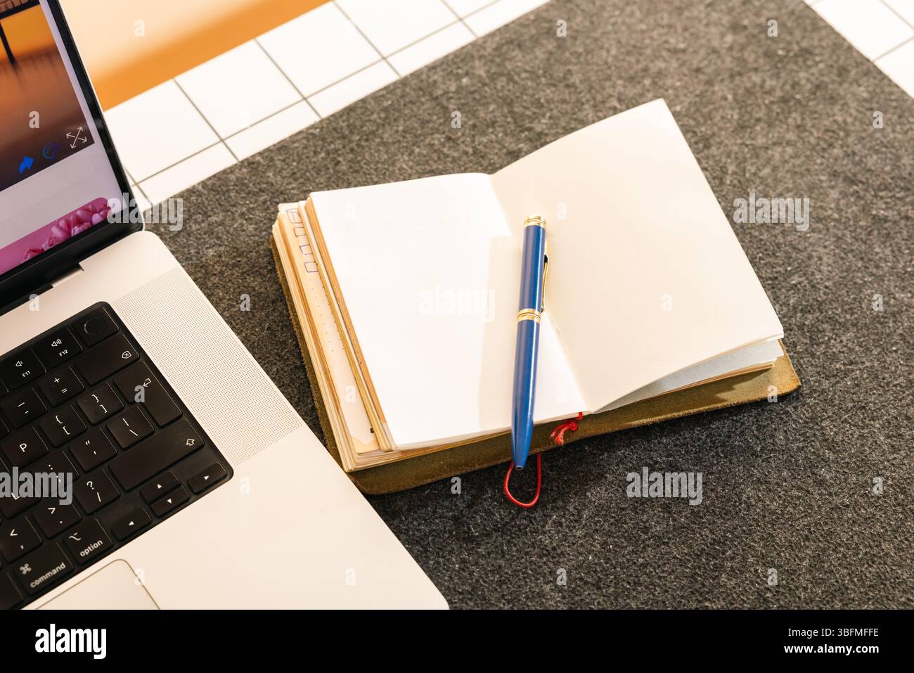 Immagine angolata di un notebook vuoto aperto e di un'elegante penna blu con finiture dorate, pronta per l'uso accanto a un notebook moderno su una scrivania ben organizzata. Questo com Foto Stock