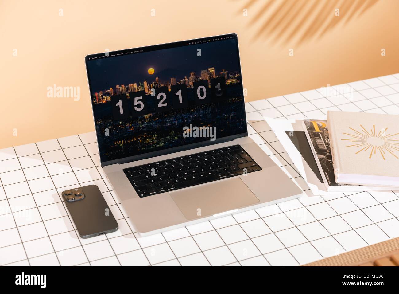 Uno spazio di lavoro contemporaneo con un laptop che visualizza una scena notturna della città con uno screensaver con orologio a scatto, insieme a uno smartphone e a libri su una griglia pa Foto Stock