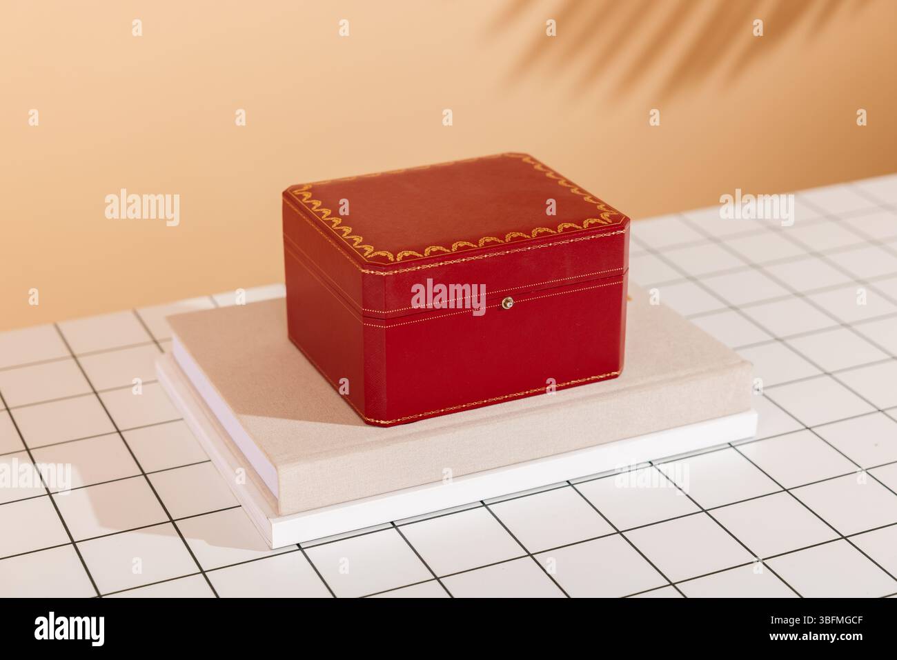 Una lussuosa confezione regalo rossa con finiture dorate, elegantemente posizionata su una pila di libri, su un moderno sfondo bianco e nero a griglia con tonalità calde Foto Stock