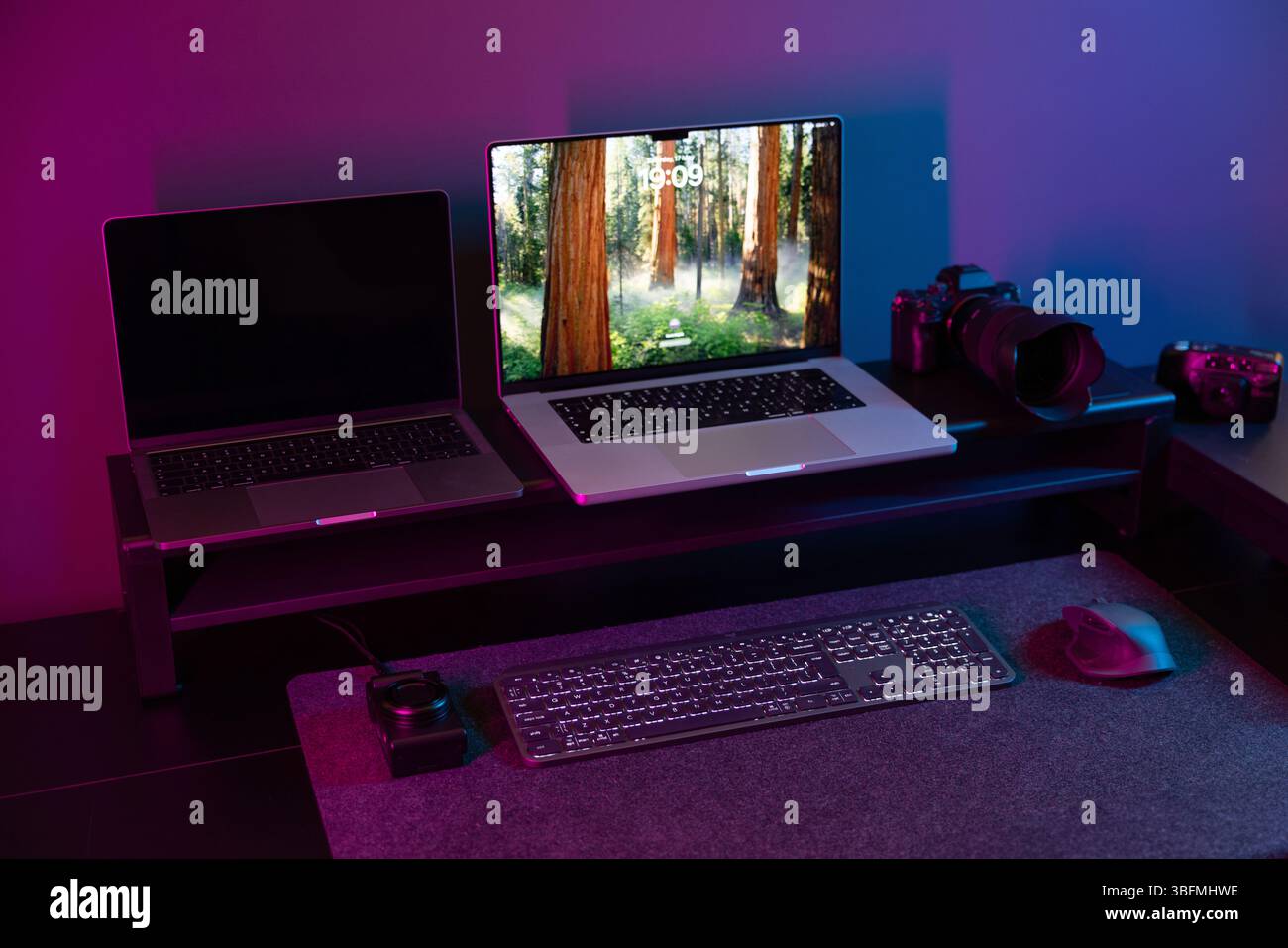 Ampia ripresa della scrivania di un creatore moderno con configurazione a due laptop su una riser, fotocamere professionali e d'epoca, tastiera e mouse, il tutto sotto immer Foto Stock