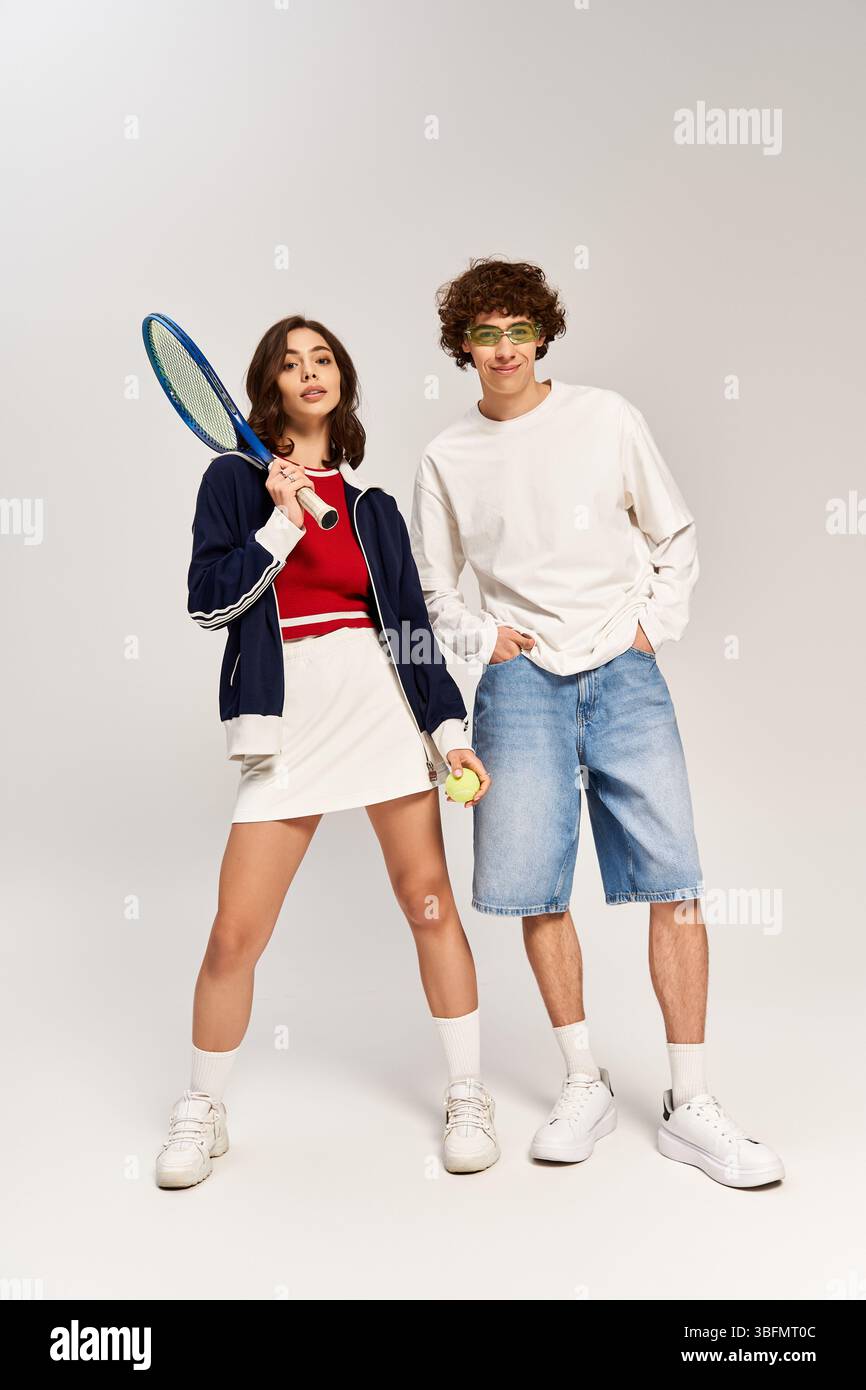 Una giovane coppia si regge con sicurezza tenendo in mano l'equipaggiamento da tennis, incarnando moda e romanticismo. Foto Stock