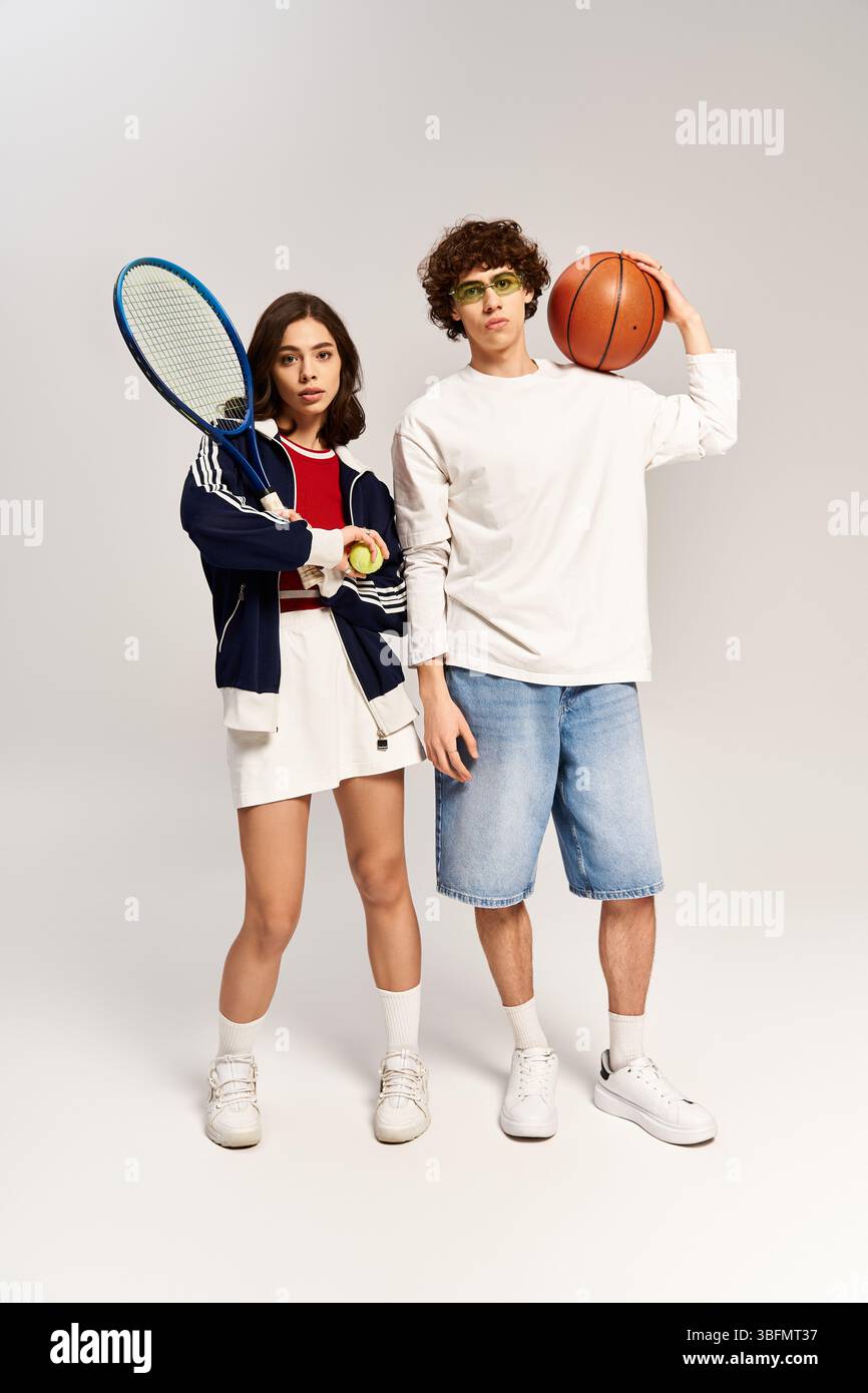 Giovane coppia elegante che trasuda amore e fiducia, pronta a indossare racchette da tennis e basket al chiuso. Foto Stock