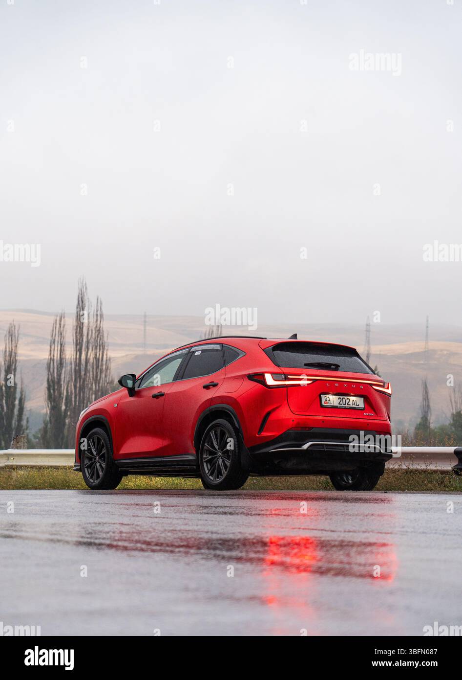 Bishkek, Kirghizistan - 12 ottobre 2024: Vista dall'angolo posteriore di un SUV Lexus NX350 rosso su una strada bagnata, con alberi lontani e un cielo nebbioso Foto Stock