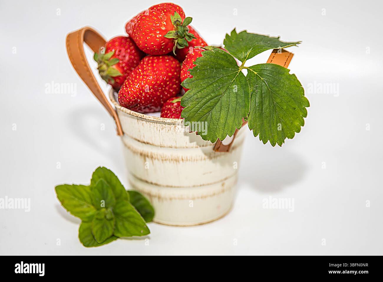 Fragole fresche con foglie di menta in secchio bianco decorativo, isolate su sfondo bianco Foto Stock