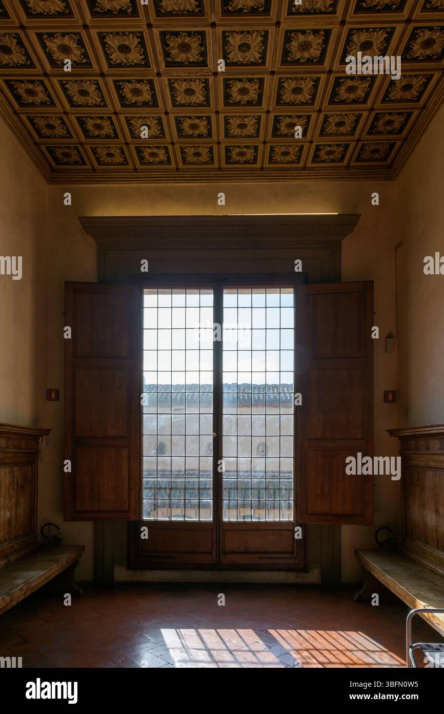 Vista interna di una sala soleggiata con una grande finestra in legno, panche intagliate e soffitto a cassettoni, secondo piano del Monastero di San Marco, Firenze, Italia. Foto Stock