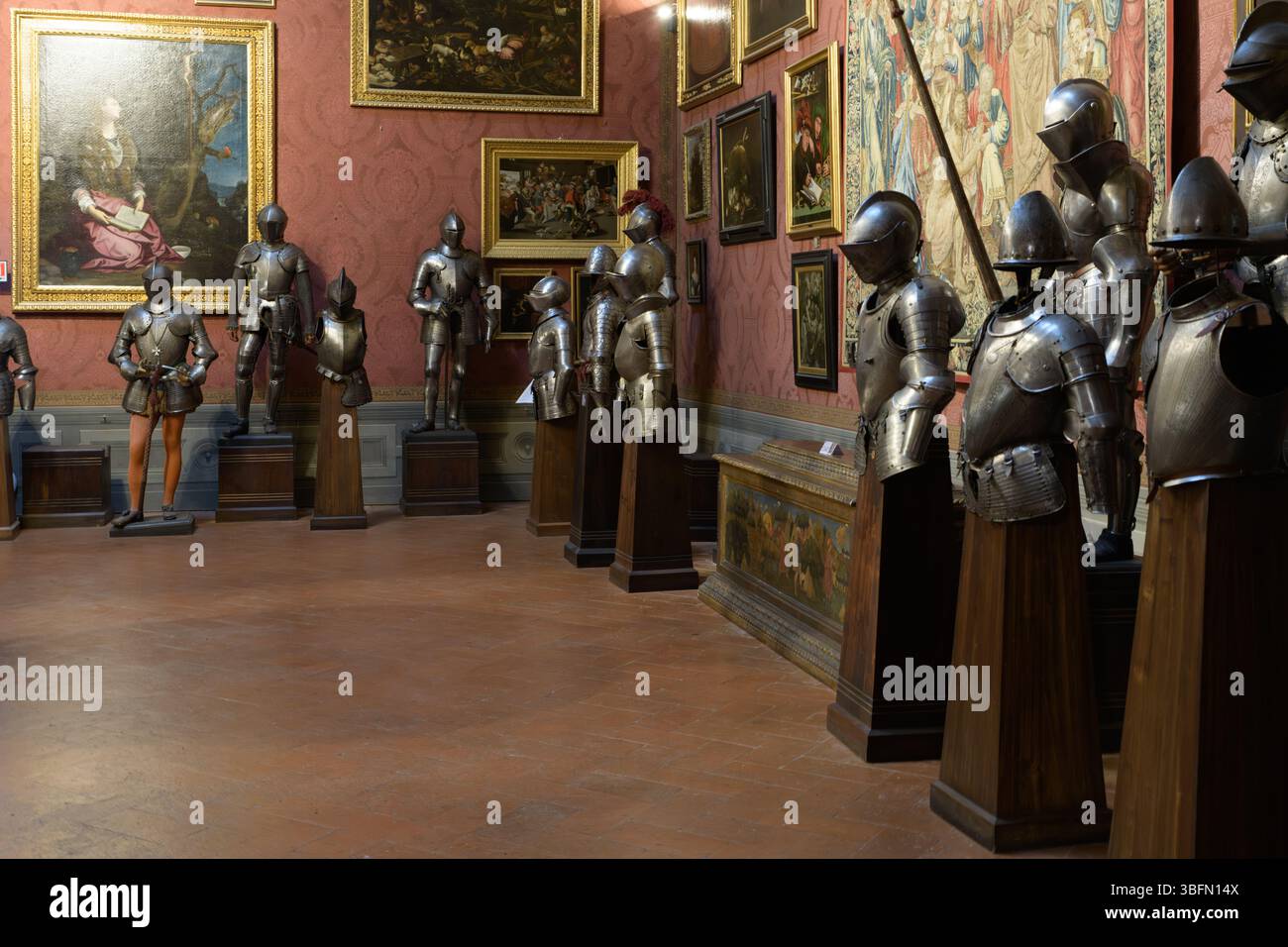 Galleria interna del Museo Stibbert di Firenze, Italia, con una collezione di armature e dipinti europei su pareti rosse damascate. Foto Stock