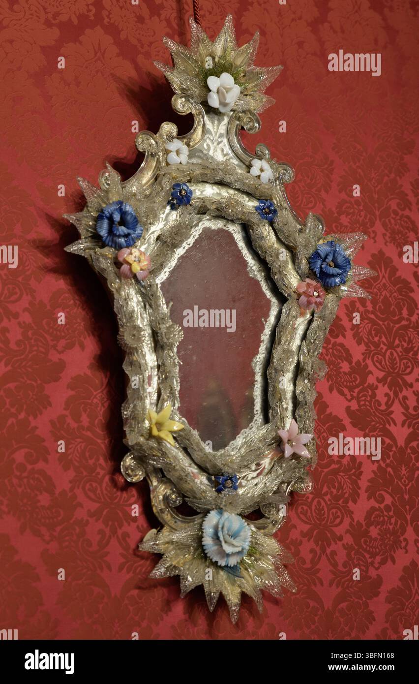 Specchio in stile barocco con decorazioni floreali in vetro di Murano su parete in damasca rossa, Museo Stibbert, Firenze, Italia. Foto Stock
