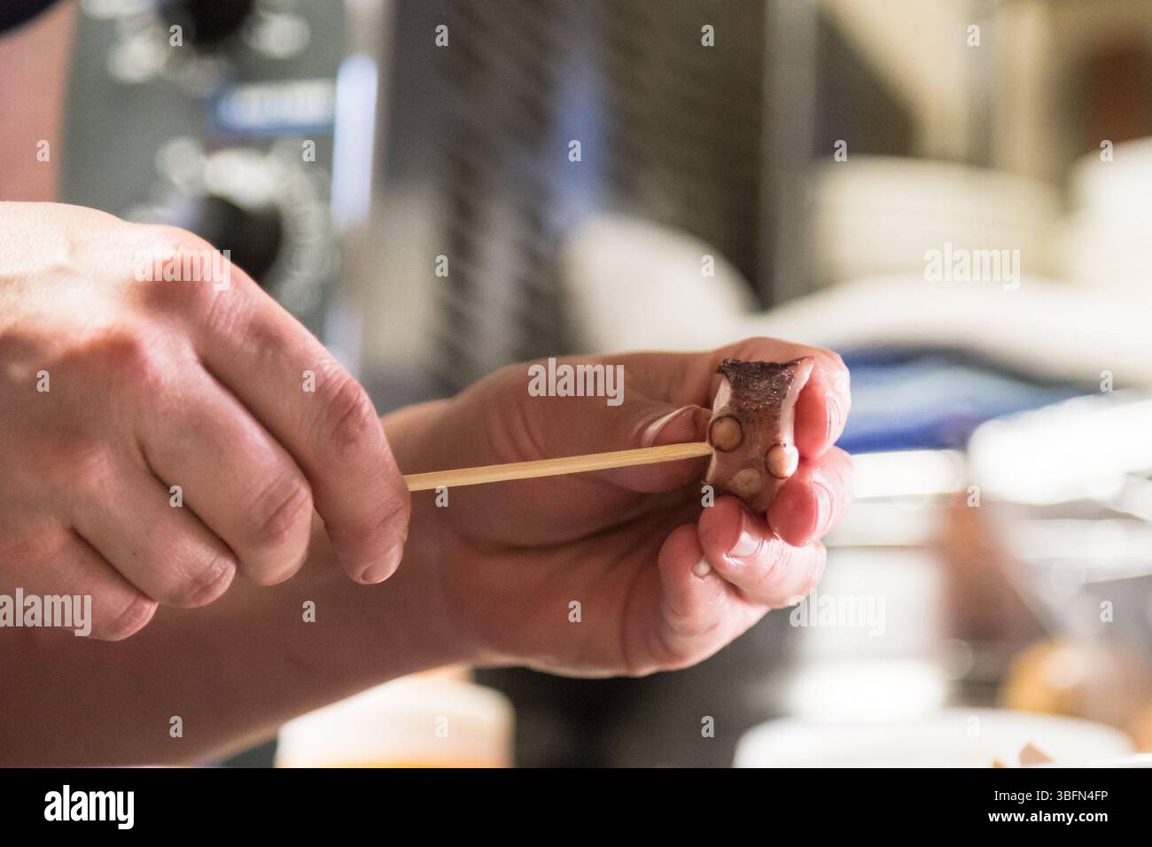 Uno chef spiedini polpo per una creazione culinaria, che mostra precisione e abilità nella preparazione del cibo. Foto Stock