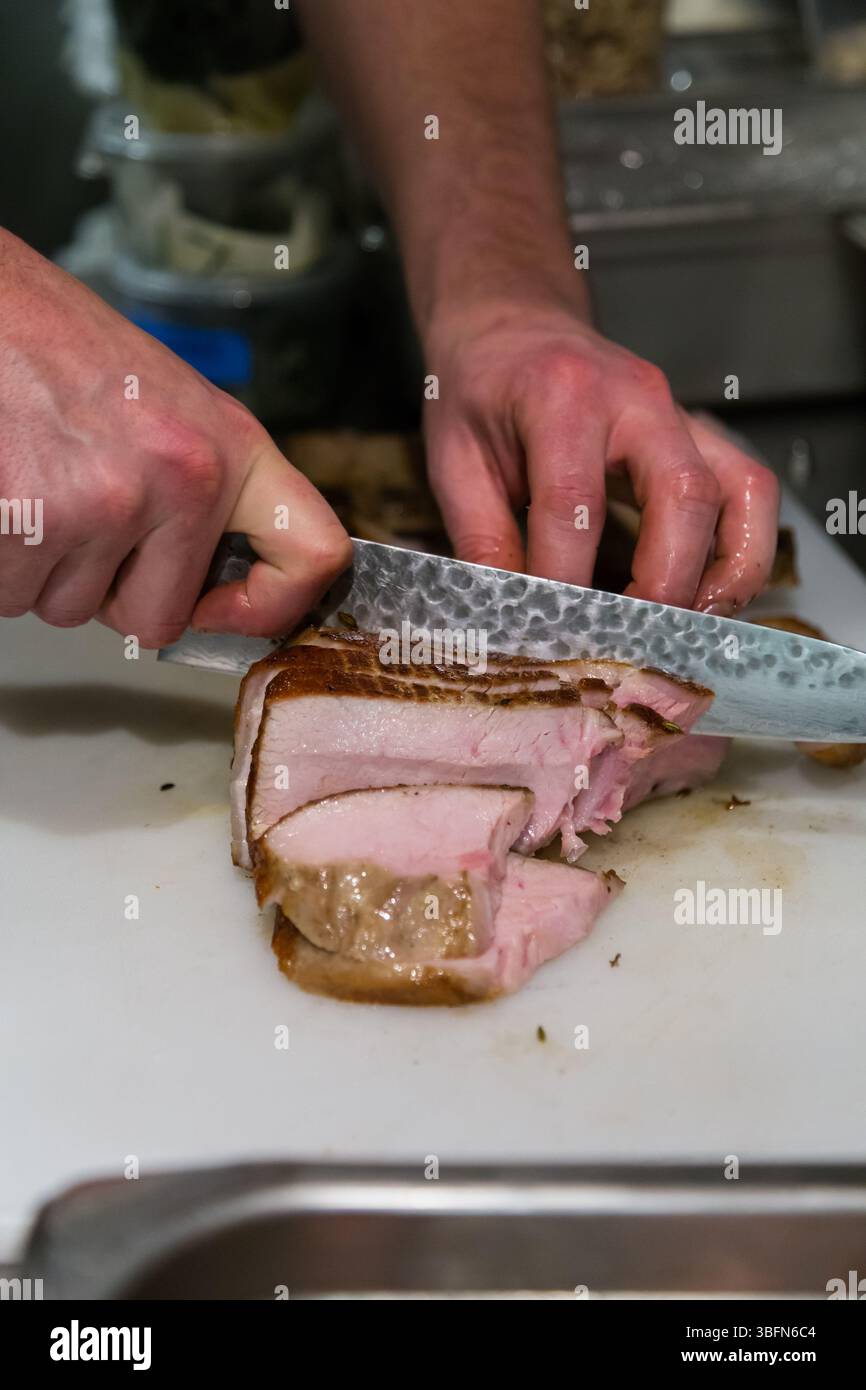 Uno chef affetta il maiale cotto su un tagliere, preparandolo per un piatto. Foto Stock