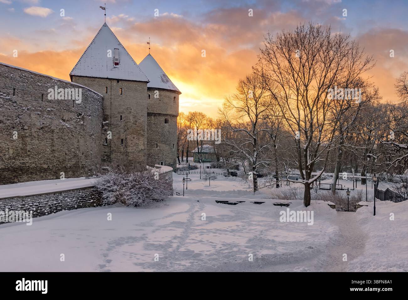 Un'ardente alba invernale riscalda le torri di pietra ricoperte di neve delle mura della città di Tallinn, l'Estonia, dove storia e natura si incontrano in tranquilla armonia. Foto Stock