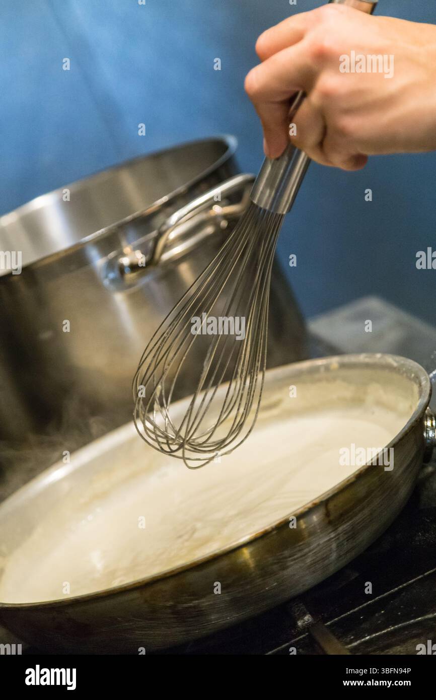 Lo chef sbatte una salsa cremosa in una padella, garantendo una consistenza omogenea per un piatto delizioso. Foto Stock