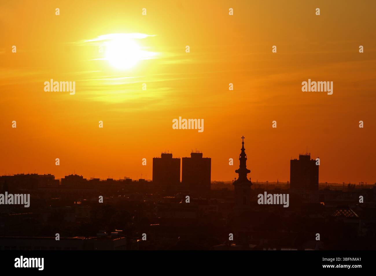 Il vivace tramonto sullo skyline della città con le silhouette di torri moderne e un campanile storico della chiesa, creando una scena drammatica dell'ora d'oro. Foto Stock