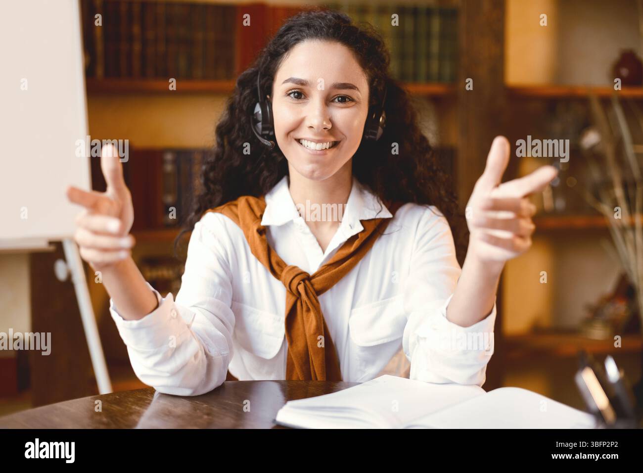 Donna seduta alla scrivania, che parla con la fotocamera indossando la cuffia Foto Stock