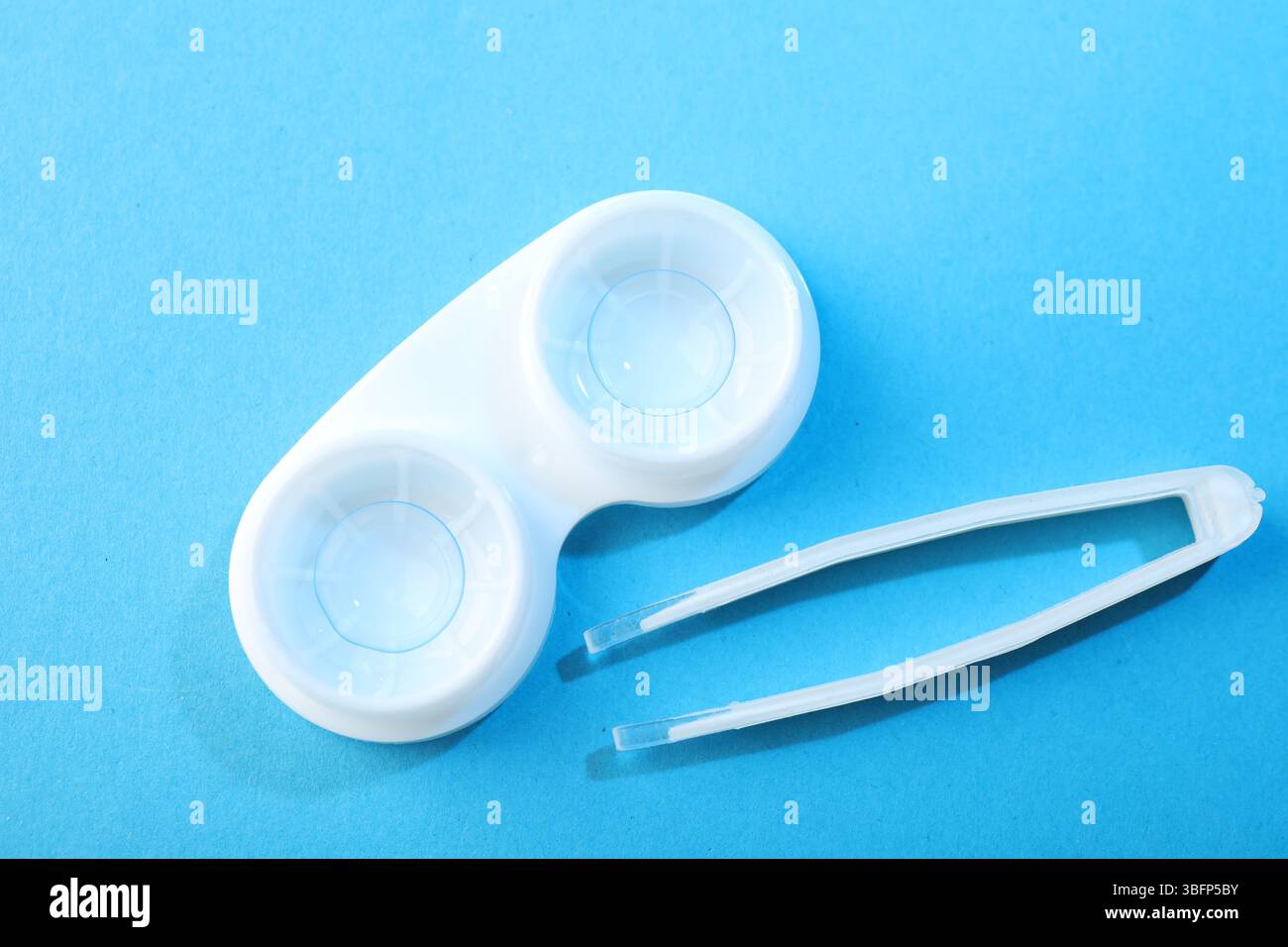 Lenti a contatto in astuccio e pinzette su sfondo blu, piatto Foto Stock