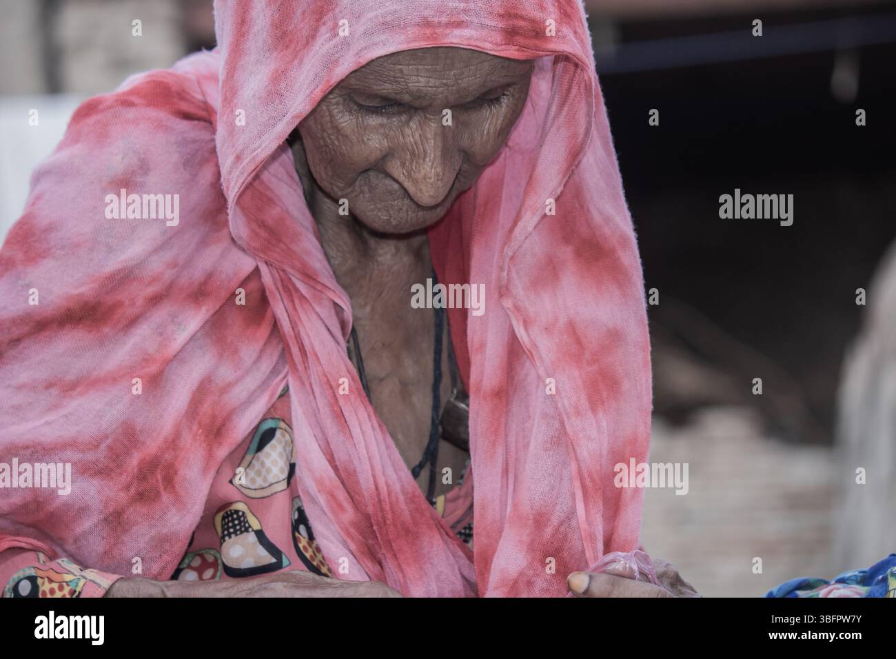 Donna anziana in abbigliamento tradizionale si concentra sul suo lavoro, mostrando la vita rurale, la saggezza e il patrimonio culturale Foto Stock