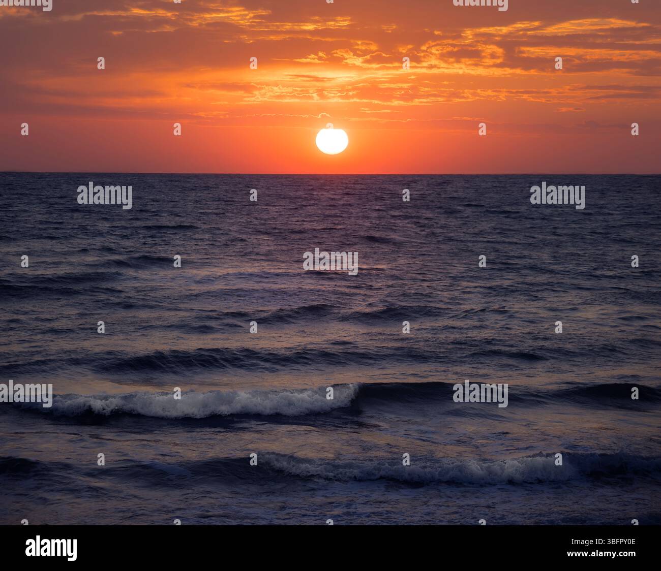 Le sfumature dorate si fondono con il mare calmo mentre il sole tramonta sulla Sicilia, gettando un magico bagliore sulle acque tranquille dell'Italia Foto Stock