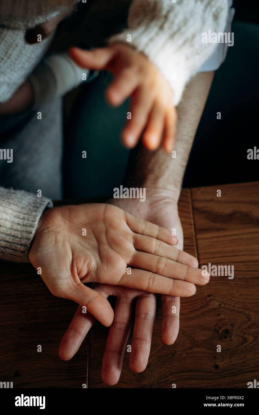 Primo piano di due mani adulte e di una mano di un bambino che si avvicinano l'una all'altra, simboleggiando il legame e la cura. L'immagine cattura calore e familiarità Foto Stock
