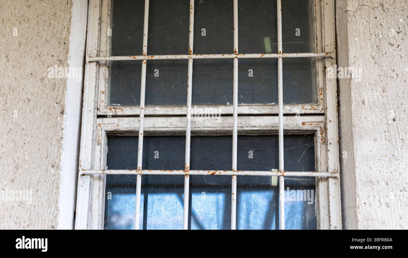 Primo piano di una finestra intemprata con barre metalliche arrugginite su una parete di cemento testurizzato, che evocano sicurezza, decadimento o abbandono. Foto Stock